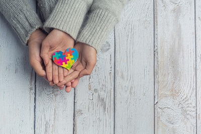 manos sujetando un corazon con colores de diversidad por el autimso