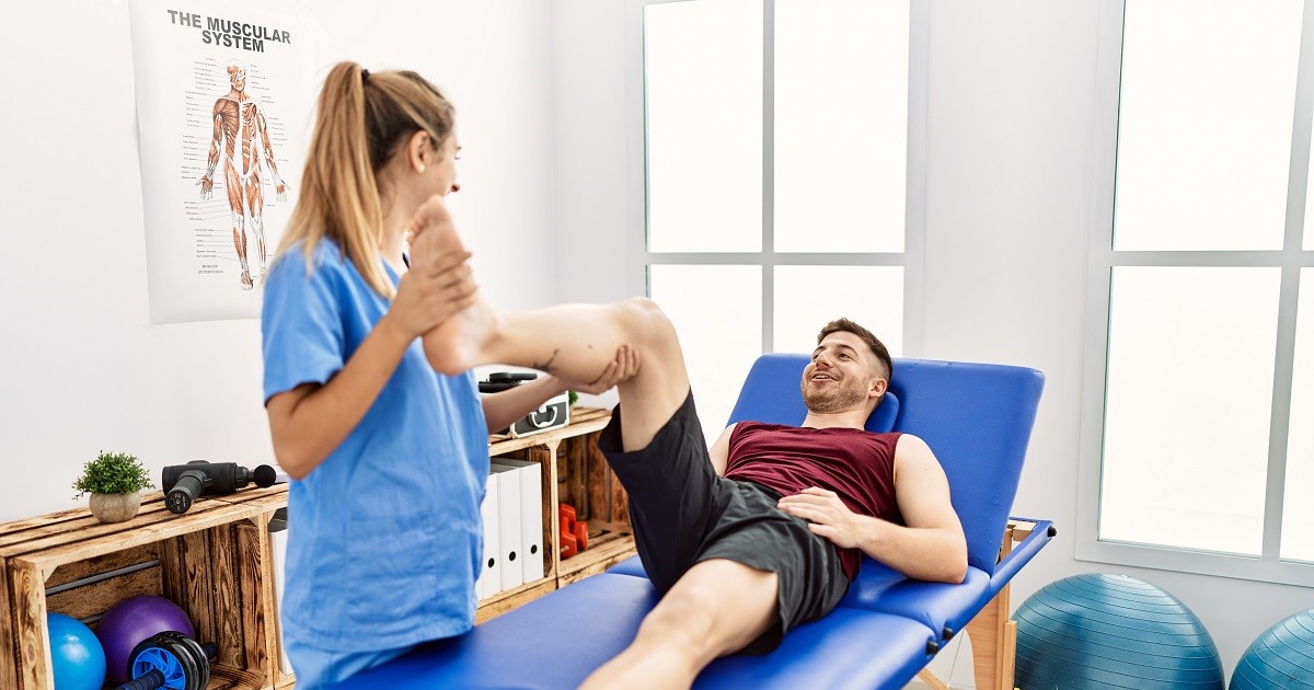mujer fisioterapia levantando la pierna de un hombre en una camilla mientras le toca el gemelo para algún tipo de molestia muscular