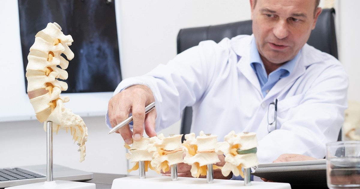 medico explicando en su consultaa traves de una maquita de la columna vertebral la osteoporosis