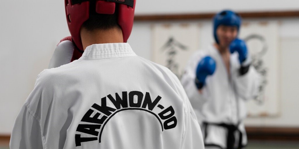 dos personas realizando taekwondo adaptado, una frente a la otra, que se ve de espaldas.