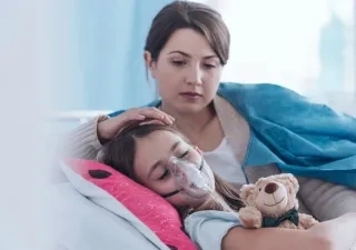 niña con una mascarilla tumbada en la cama al lado de su madre mientras la niña sufre fibrosis quítica