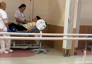 En un box de un hospital, una doctora y una enfermera hablan con una paciente encamada